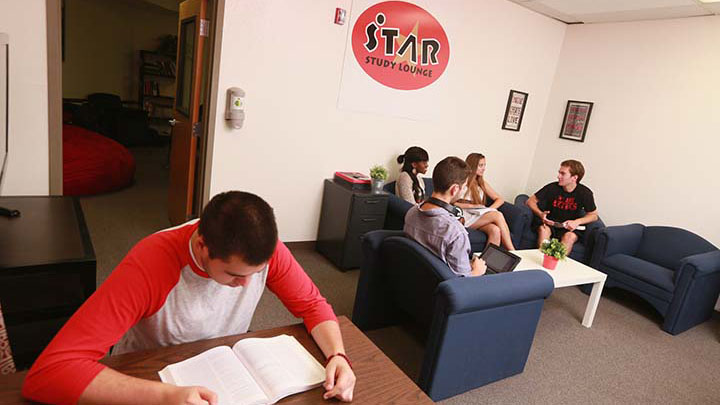 One student reads at a table, four other students hold a discussion in the STAR Study Center