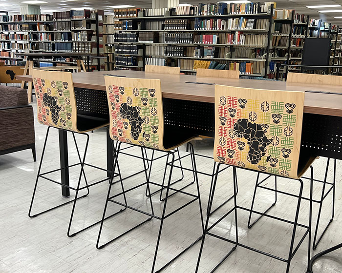 Three high chairs featuring different Adinkra symbol etchings on the back.