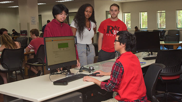 A Library Student assistant helps three other students at the 24/7 Desk