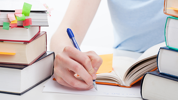 Person writing with a stack of books