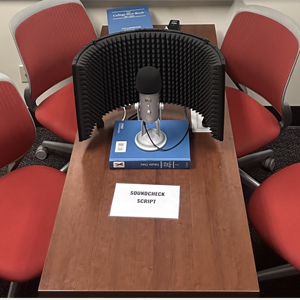 DIY podcasting setup with a microphone, pop filter, and soundcheck script surrounded by red chairs in a small room.
